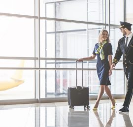 Handsome male pilot and attractive female flight attendant are walking in airport terminal together.