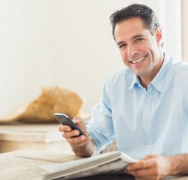 Portrait of a smiling casual man with newspaper and cellphone in the kitchen at home