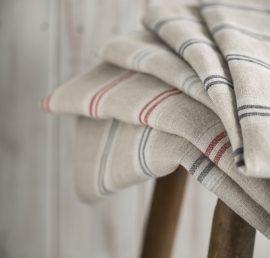 A pile of five striped linen on a wooden stool over a wooden panel background.